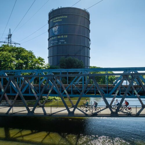 Das Foto zeigt Radfahrende auf dem Radweg entlang des Rhein-Herne-Kanals am Gasometer Oberhausen