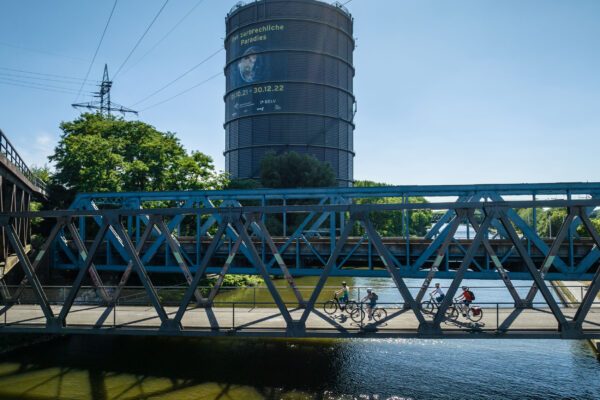 Das Foto zeigt Radfahrende auf dem Radweg entlang des Rhein-Herne-Kanals am Gasometer Oberhausen