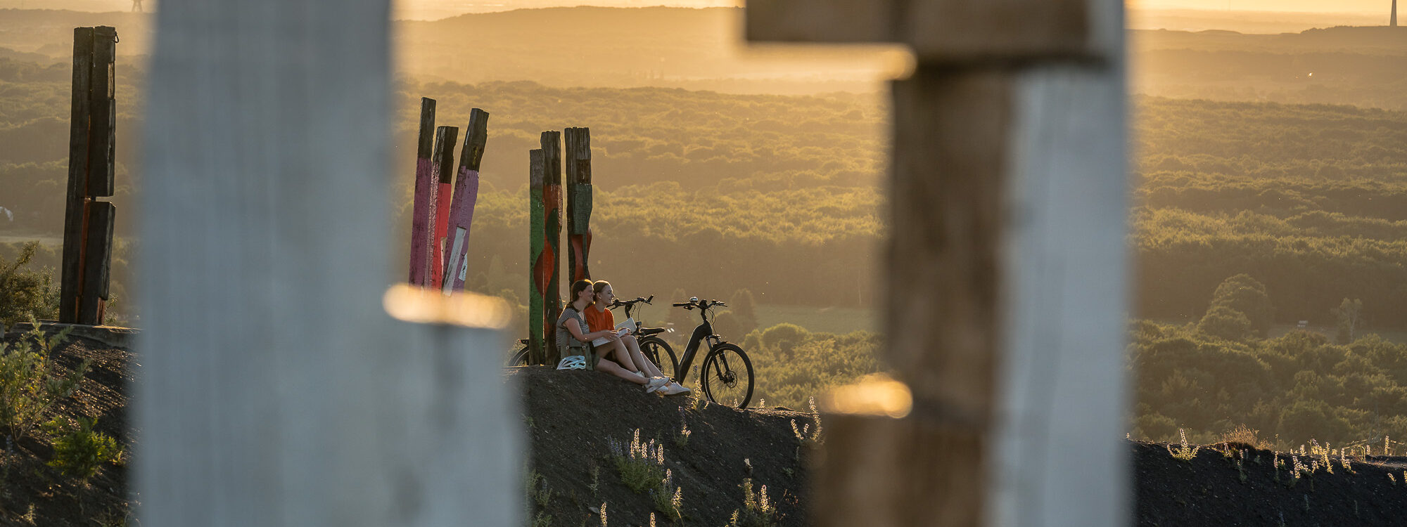 Das Foto zeigt zwei Radfahrerinnen beim Sonnenuntergang auf der Halde Haniel in Bottrop