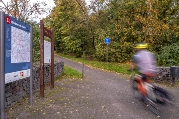 Das Foto zeigt einen Radfahrer auf der HOAG-Trasse in Duisburg auf Höhe einer Knotenpunkttafel auf der RevierRoute Stahlküche