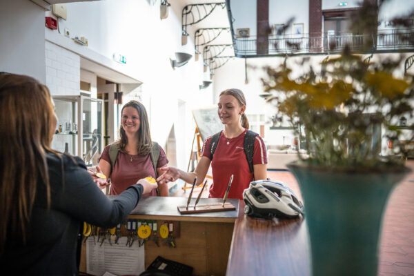 Das Foto zeigt zwei Radfahrerinnen beim Check in im Bett + Bike Hotel Alte Lohnhalle in Essen