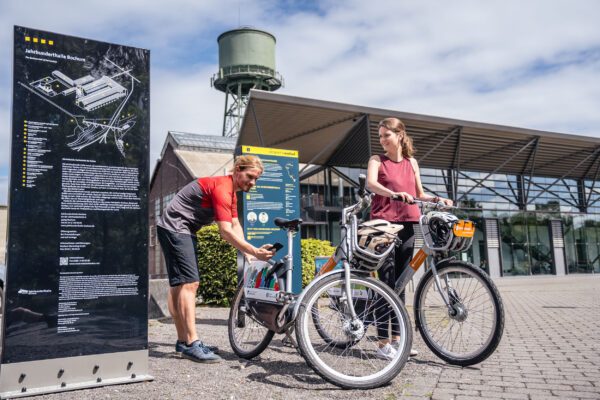 Das Foto zeigt zwei Radfahrende an der metropolradruhr Station an der Jahrhunderthalle Bochum auf der Route Industriekultur