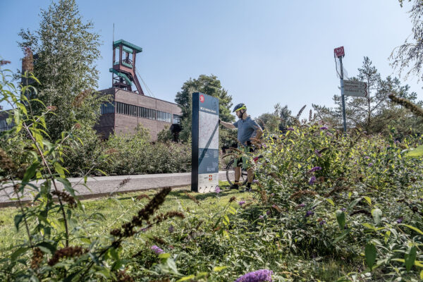 Das Foto zeigt einen Radfahrer auf dem Gelände des UNESCO-Welterbe Zollverein in Essen an der Knotenpunkttafel des Knotenpunkts 59 auf der RevierRoute Grubenfahrt