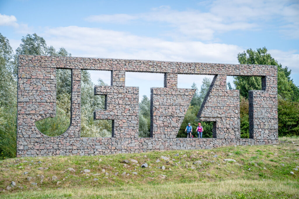 Das Foto zeigt Radfahrende auf dem Radweg entlang der Seseke vorm Kunstwerk "Jetzt" in Kamen