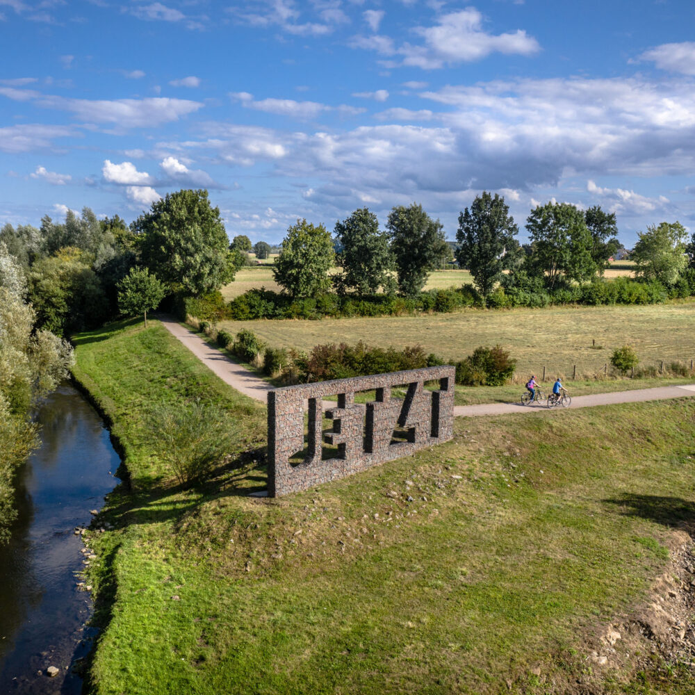 Das Foto zeigt Radfahrende auf dem Radweg entlang der Seseke vorm Kunstwerk "Jetzt" in Kamen