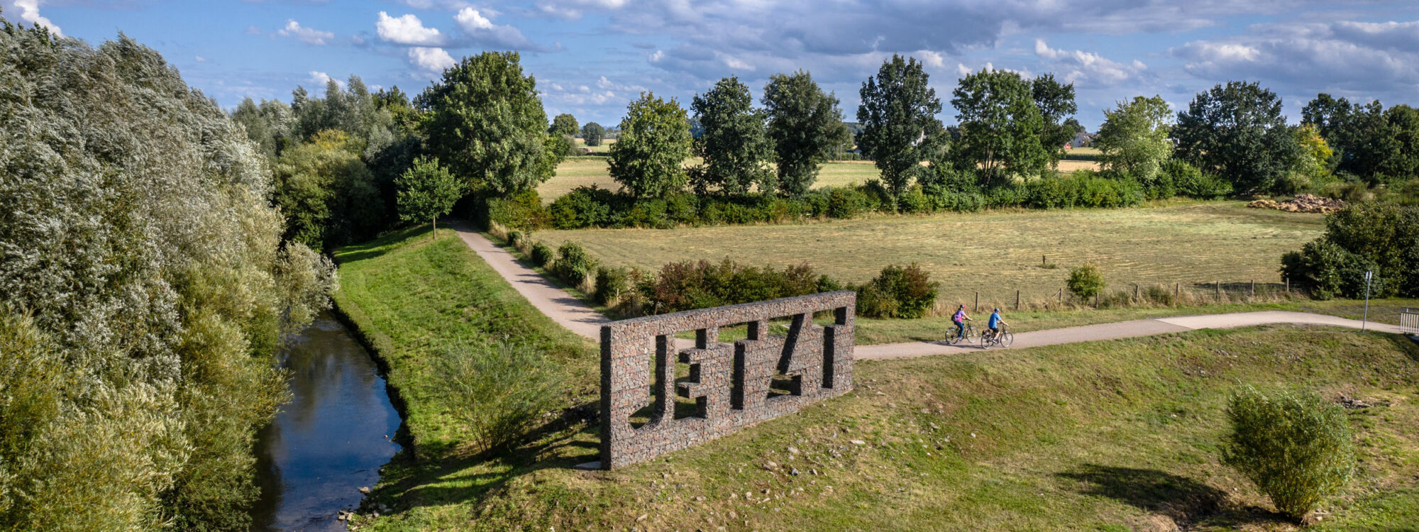 Das Foto zeigt Radfahrende auf dem Radweg entlang der Seseke vorm Kunstwerk "Jetzt" in Kamen