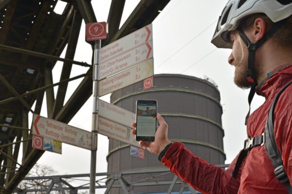 The photo shows a cyclist with the digital radtourenplaner.ruhr on his cell phone