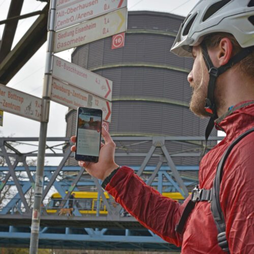 Das Foto zeigt einen Radfahrer am Gasometer Oberhausen mit dem radtourenplaner.ruhr auf dem Handy