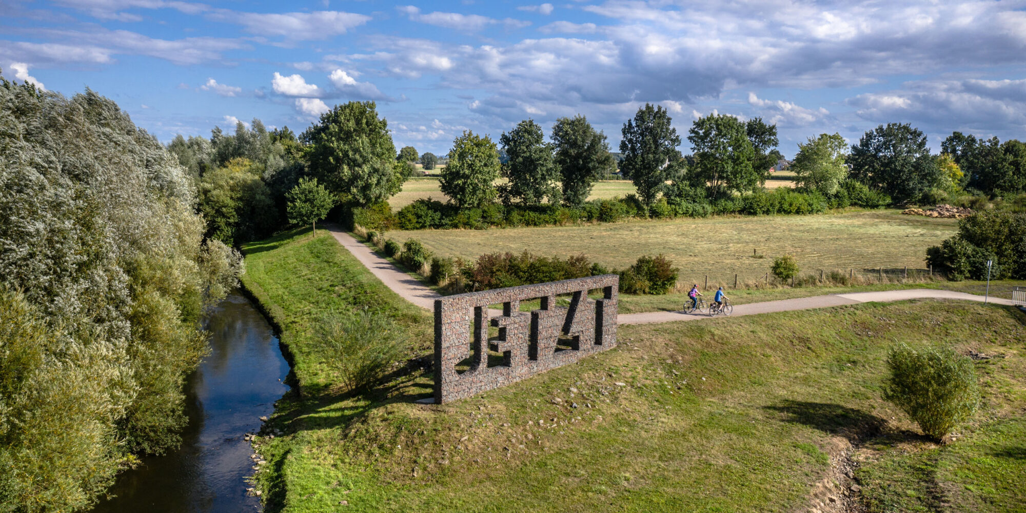 Das Foto zeigt Radfahrende auf dem Radweg entlang der Seseke vorm Kunstwerk "Jetzt" in Kamen