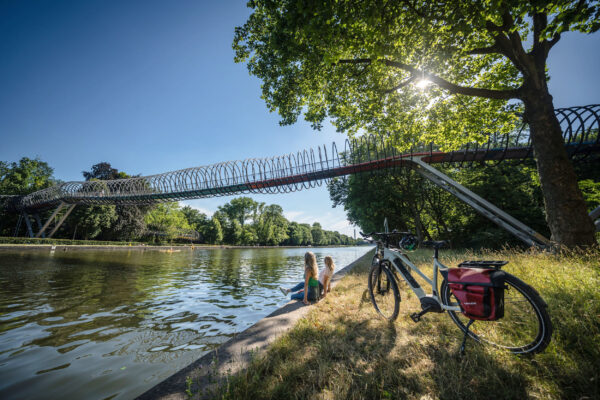 Das Foto zeigt zwei Radfahrerinnen am Ufer des Rhein-Herne-Kanals vor der Brücke Slinky Springs to Fame in Oberhausen