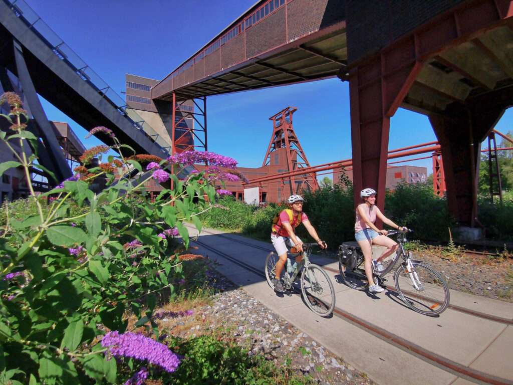 Das Foto zeigt zwei Radfahrende am UNESCO-Welterbe Zollverein in Essen auf der RevierRoute Grubenfahrt