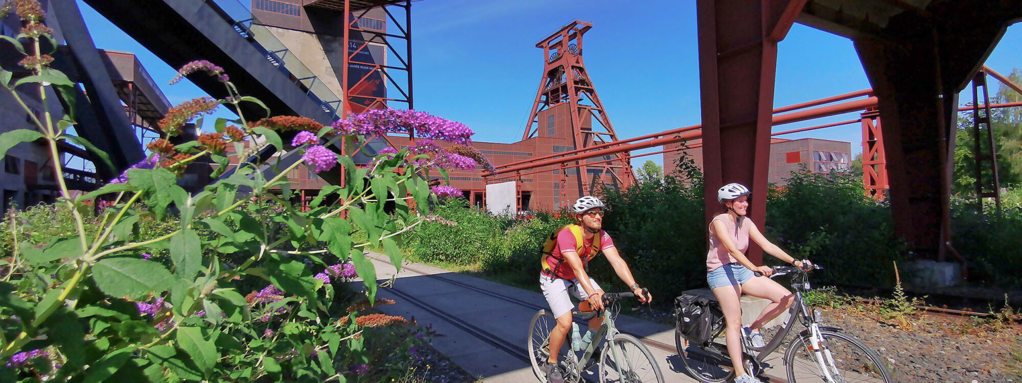 Das Foto zeigt zwei Radfahrende am UNESCO-Welterbe Zollverein in Essen auf der RevierRoute Grubenfahrt