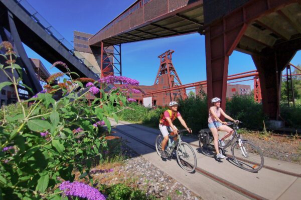 Das Foto zeigt zwei Radfahrende am UNESCO-Welterbe Zollverein in Essen auf der RevierRoute Grubenfahrt