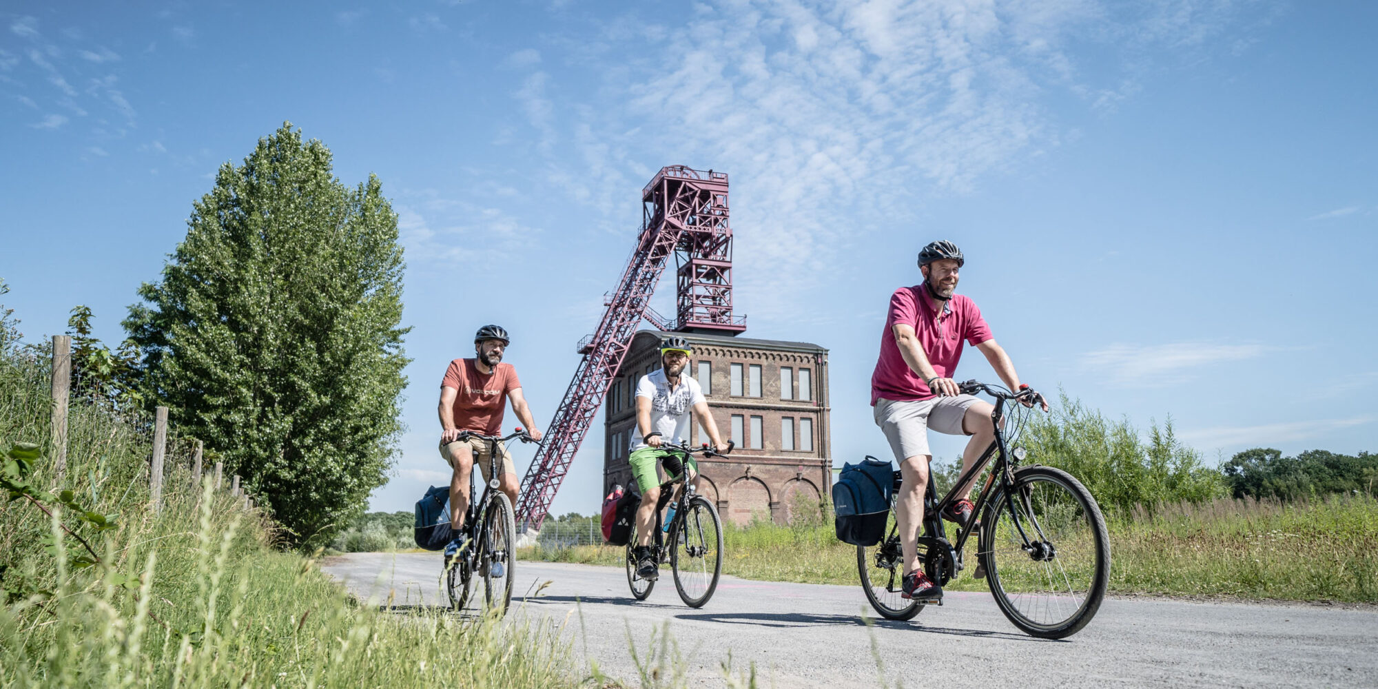 The photo shows three cyclists cycling along the HOAG route in Oberhausen in front of the Sterkrade colliery on the Steel Kitchen RevierRoute