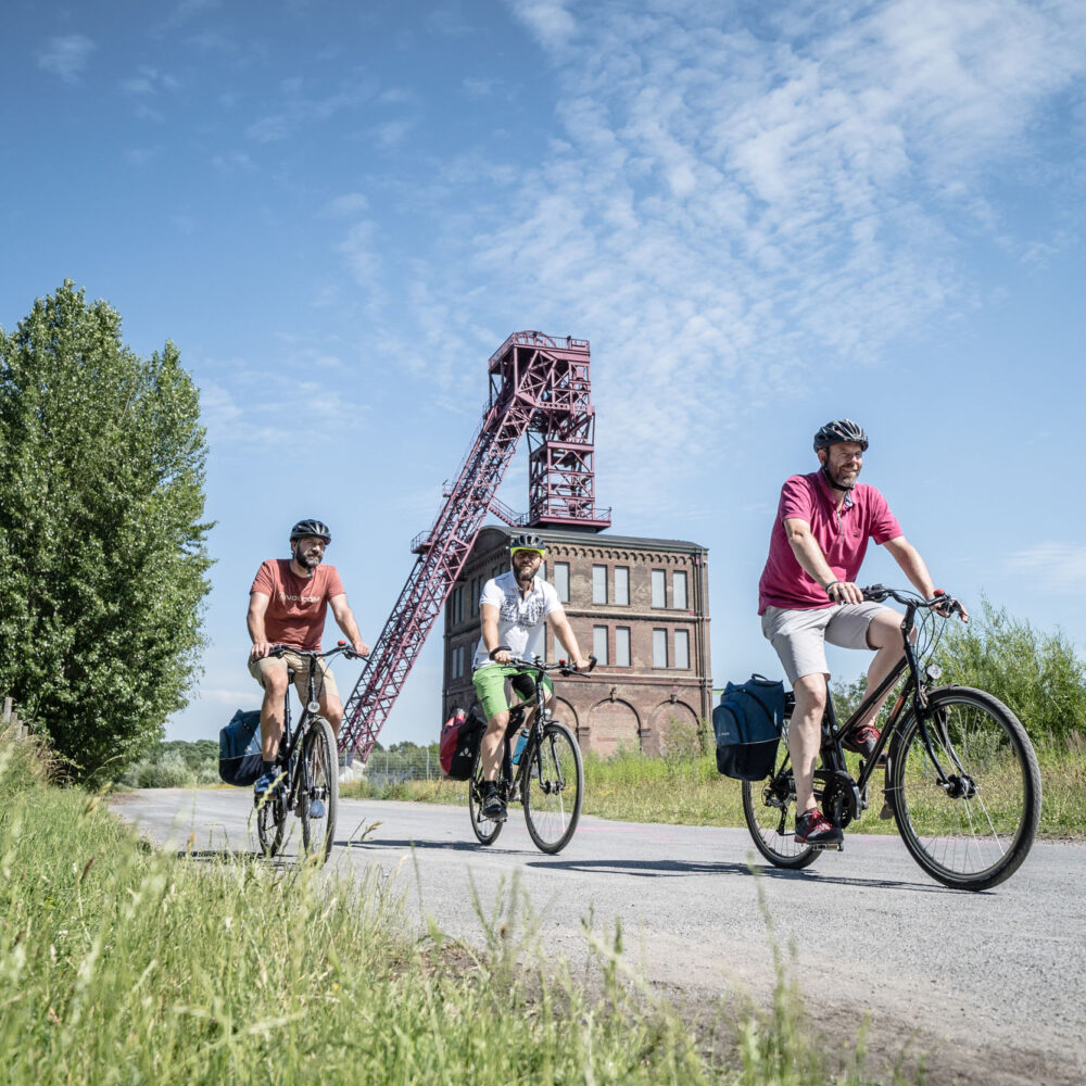 Das Foto zeigt drei Radfahrer beim Bahntrassenradeln auf der HOAG-Trasse in Oberhausen vor der Zeche Sterkrade bei der RevierRoute Stahlküche
