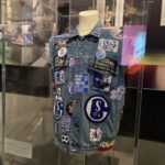 Eine ärmellose Jeansweste, die mit verschiedenen blauen, weißen und roten gestickten Aufnähern bedeckt ist, von denen viele das Logo und die Farben des deutschen Fußballvereins FC Schalke 04 zeigen, wird auf einer Schaufensterpuppe in einer Museumsausstellung ausgestellt.