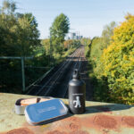 Das Bild zeigt ein Butterbrot und eine Trinkflasche auf einer Eisenbahnbrücke