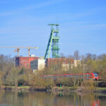 Das Foto zeigt auf der anderen Uferseite der Ruhr die Zeche Heinrich, die Radfahrer auf ihrer Tour durchs radrevier.ruhr auf dem RuhrtalRadweg erblicken.